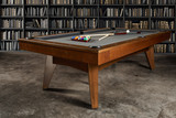 Full view of the Doc & Holliday Scholar Slate Pool Table in pecan finish, shown in a 3/4 angle within a styled lifestyle setting — featuring the luxury billiard ball set and cue sticks placed across the playing surface, capturing the spirit of refined American recreation.