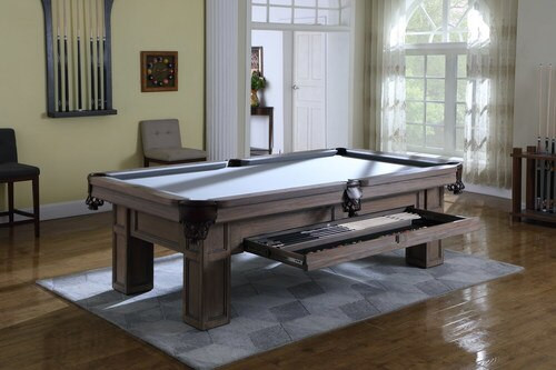 A lifestyle scene showing the integrated pull-out storage drawer in use, filled with cues, balls, and triangle—demonstrating the table’s smart, space-saving design.