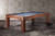 Captured in a styled interior, this ¾ lifestyle shot features the Alta Slate Pool Table in its exclusive Honey Ash finish. The Parsons-style frame is grounded yet minimalist, while the warm wood tone brings light and texture to the space. Made by American Heritage Billiards and available only at Sawyer Twain, this table blends performance and design effortlessly.