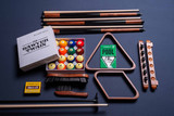 Shot directly on Championship billiard felt, this lifestyle photo places the cues, chalk, triangle rack, and bridge stick in their element—ready for action. The layout feels effortless, with premium details like the brown-stained cue butts and vibrant blue chalk adding a subtle richness to the scene.
