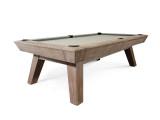 Three-quarter lifestyle view of the Nixon Desyn Pool Table in Antique finish, styled in a rustic contemporary interior with warm textures and industrial accents. Highlights the clean leg design, rich finish, and how seamlessly the table integrates into a thoughtfully designed space.
