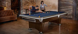 A dynamic lifestyle shot of friends enjoying a game of pool on the Brunswick Gold Crown VI in Skyline Walnut finish. The sleek, modern design is complemented by brushed nickel accents and a flawless playing surface, offering both style and professional-grade performance. This image captures the excitement and sophistication of luxury game rooms—where family and friends gather for both fun and competition.